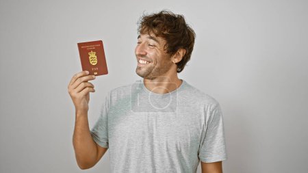 Téléchargez les photos : Joyeux jeune homme passe avec confiance son passeport danois avec un sourire, isolé sur fond blanc. un voyageur décontracté et heureux du Danemark, prêt pour son aventure européenne. - en image libre de droit