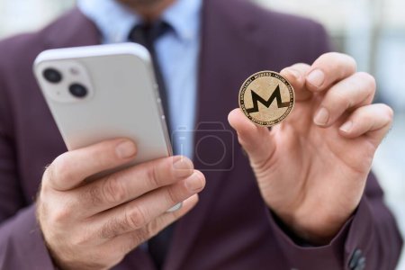 Téléchargez les photos : Homme d'âge moyen travailleur d'affaires tenant monero crypto monnaie en utilisant un smartphone à la rue - en image libre de droit