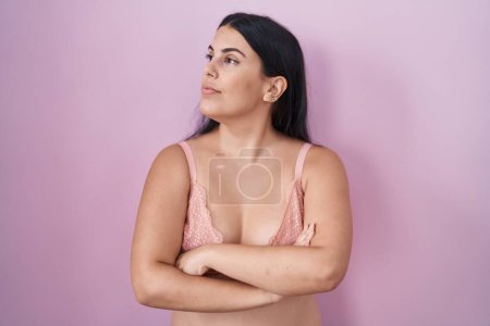 Téléchargez les photos : Jeune femme hispanique portant un soutien-gorge rose regardant sur le côté avec les bras croisés convaincus et confiants - en image libre de droit