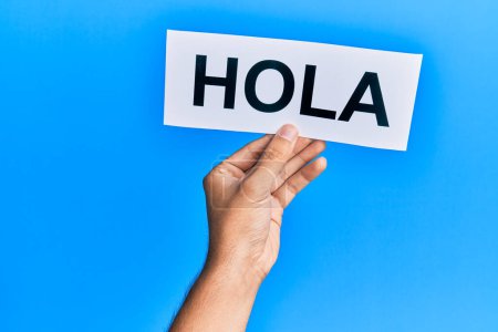 Hand of caucasian man holding paper with hola word over isolated blue background