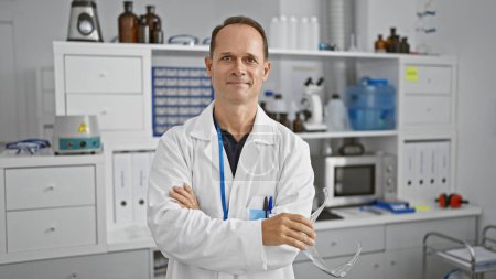 Foto de Hombre de mediana edad, un científico feliz, sonriendo con los brazos cruzados mientras está de pie en su laboratorio - Imagen libre de derechos