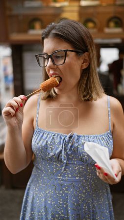 Hispanic woman in glasses savoring delicious breaded cheese stick on the traditional streets of kyoto
