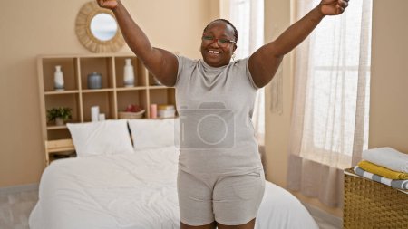 Photo for Confident african american woman, smiling with arms raised up in celebration, standing in her bedroom on a cheerful morning - Royalty Free Image
