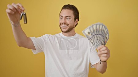Photo for Young hispanic man pointing to key of new car holding dollars over isolated yellow background - Royalty Free Image
