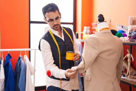 Photo for Young hispanic man tailor drinking coffee standing by manikin at atelier - Royalty Free Image