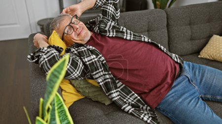 A cheerful grey-haired man relaxing on a sofa in a cozy living room, exuding comfort and joy.