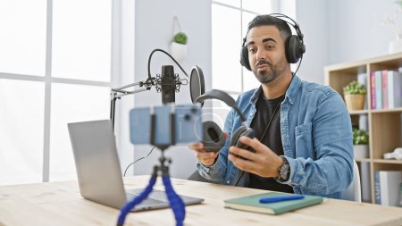 Téléchargez les photos : Homme hispanique avec barbe accueillant podcast en studio moderne, ordinateur portable et microphone sur la table. - en image libre de droit