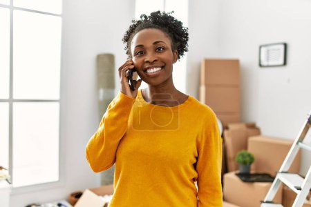 Téléchargez les photos : Femme afro-américaine parlant sur smartphone debout à la nouvelle maison - en image libre de droit