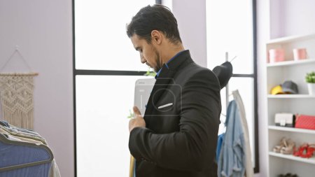 Hombre hispano guapo ajustando traje en vestidor moderno con perchero y espejo.