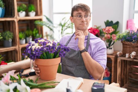 Foto de Hombre rubio caucásico trabajando en floristería pensando preocupado por una pregunta, preocupado y nervioso con la mano en la barbilla - Imagen libre de derechos