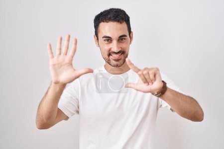 Photo for Handsome hispanic man standing over white background showing and pointing up with fingers number seven while smiling confident and happy. - Royalty Free Image