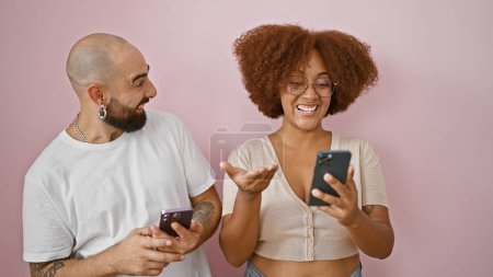 Téléchargez les photos : Beau couple souriant, debout ensemble sur fond rose isolé, profitant de textos sur smartphones, exsudant confiance et amour - en image libre de droit