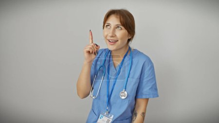 Foto de Una profesional de la salud femenina en uniformes azules con un estetoscopio apuntando hacia arriba, aislada sobre un fondo blanco. - Imagen libre de derechos