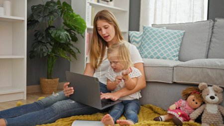 Zu Hause sitzen eine entspannte kaukasische Mutter und ihre Tochter zusammen, vertieft in einen Film auf dem Laptop, gemütlich auf dem Wohnzimmerboden.
