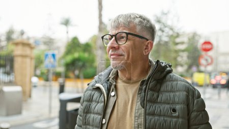 Photo for Middle-aged man with grey hair and glasses smiling outdoors on an urban street. - Royalty Free Image