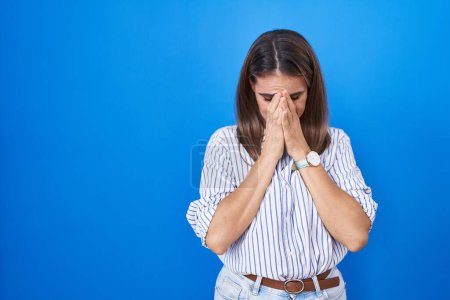 Foto de Mujer joven hispana de pie sobre fondo azul con expresión triste cubriendo la cara con las manos mientras llora. concepto de depresión. - Imagen libre de derechos