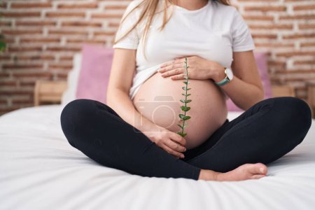 Foto de Mujer embarazada joven tocando la planta de retención del vientre en el dormitorio - Imagen libre de derechos