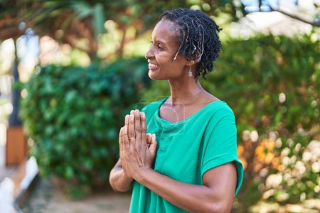 Téléchargez les photos : Moyen Age femme afro-américaine souriante confiante faire de l'exercice de yoga au parc - en image libre de droit