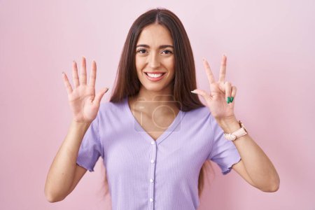 Photo for Young hispanic woman with long hair standing over pink background showing and pointing up with fingers number eight while smiling confident and happy. - Royalty Free Image