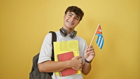 Foto de Joven estudiante hispano confiado, un muchacho patriótico sosteniendo su bandera cubana y libros aislados sobre un vibrante telón de fondo amarillo! - Imagen libre de derechos