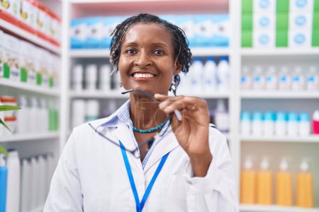 Foto de Farmacéutica afroamericana de mediana edad sonriendo confiada de pie en la farmacia - Imagen libre de derechos