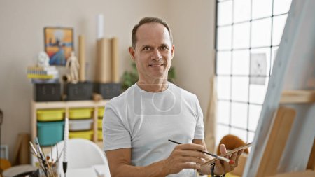 Photo for Confident middle age man, a smiling artist, thoroughly enjoys drawing in his studio, channeling his inner creativity - Royalty Free Image