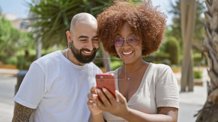 Téléchargez les photos : Beau couple, riant et en confiance debout ensemble dans une rue de la ville, souriant et collant sur des messages partagés sur leur smartphone - en image libre de droit