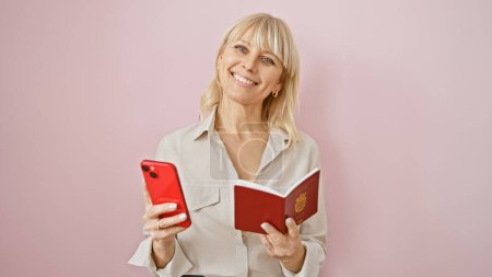 Mujer rubia con pasaporte danés y teléfono inteligente sonríe sobre un fondo rosa
