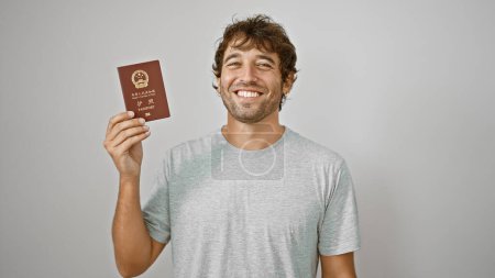 Téléchargez les photos : Portrait d'un jeune homme beau et souriant rayonnant de confiance, tenant joyeusement son passeport pour la Chine, debout isolé sur un fond blanc, prêt pour son aventure de vacances - en image libre de droit