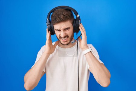 Téléchargez les photos : Homme hispanique avec barbe écoutant de la musique portant des écouteurs couvrant les oreilles avec des doigts avec une expression agacée pour le bruit de la musique forte. concept sourd. - en image libre de droit