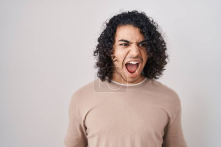 Téléchargez les photos : Homme hispanique avec les cheveux bouclés debout sur fond blanc en colère et fou hurlant frustré et furieux, criant de colère. rage et concept agressif. - en image libre de droit