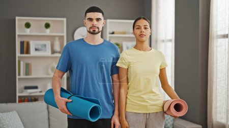 Photo for Stunningly athletic couple hold yoga mat, standing in serious concentration in their home's living room, showcasing a lifestyle of health, fitness and love. - Royalty Free Image