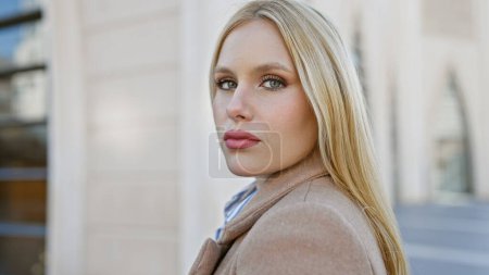 Téléchargez les photos : Une jeune femme blonde séduisante pose élégamment dans une rue de la ville, exsudant beauté et sophistication urbaine. - en image libre de droit