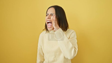 Foto de Mujer hispana joven gritando sobre un sólido fondo amarillo, retratando la emoción con un estilo casual. - Imagen libre de derechos