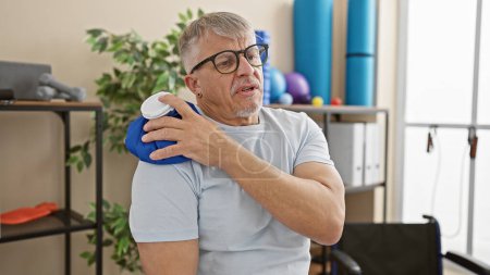 Photo for Mature man in clinics rehabilitation room using ice pack on shoulder - Royalty Free Image