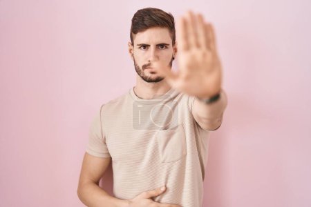 Photo for Hispanic man with beard standing over pink background doing stop sing with palm of the hand. warning expression with negative and serious gesture on the face. - Royalty Free Image