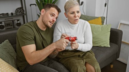 Photo for A woman and man playing video games together on a cozy sofa in a modern living room, expressing excitement and concentration. - Royalty Free Image