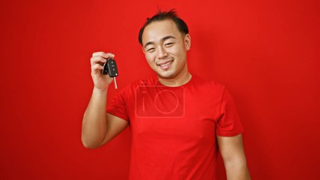 Foto de Joybursting, guapo joven asiático hombre con confianza sonriendo, de pie sobre fondo rojo, disfruta sosteniendo nueva llave del coche - Imagen libre de derechos