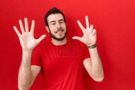 Photo for Young hispanic man wearing casual red t shirt showing and pointing up with fingers number eight while smiling confident and happy. - Royalty Free Image