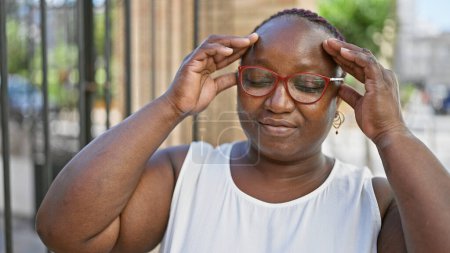 Téléchargez les photos : Femme afro-américaine stressée avec des tresses, ressentant des maux de tête dans la rue urbaine, montrant l'expression du désespoir - en image libre de droit