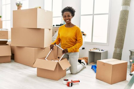 African american woman smiling confident unpacking cardboard box at new home