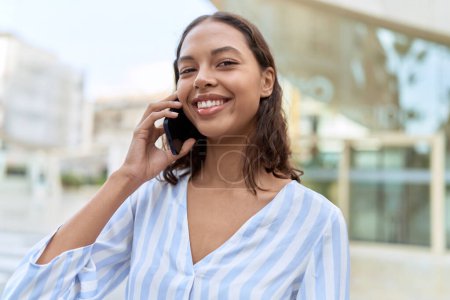 Foto de Joven mujer afroamericana sonriendo confiada hablando en el teléfono inteligente en la calle - Imagen libre de derechos