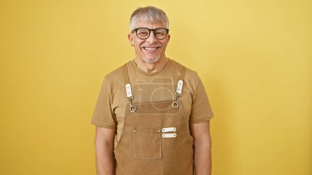 Photo for A smiling senior man with grey hair and glasses, dressed in casual clothes, stands against a vibrant yellow background. - Royalty Free Image