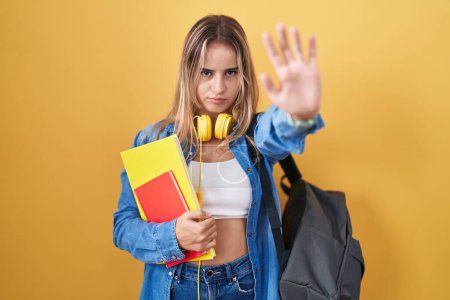 Photo for Young blonde woman wearing student backpack and holding books doing stop sing with palm of the hand. warning expression with negative and serious gesture on the face. - Royalty Free Image