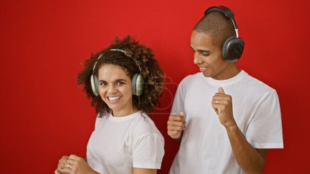 Beautiful couple in love, laughing and bonding over listening to music, dancing together on an isolated red background emitting positive vibes and confidence