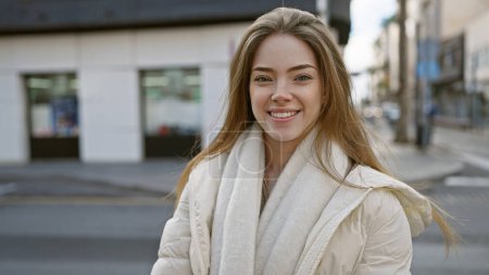 Foto de Una hermosa joven caucásica con el pelo rubio sonríe al aire libre en una calle urbana de la ciudad. - Imagen libre de derechos