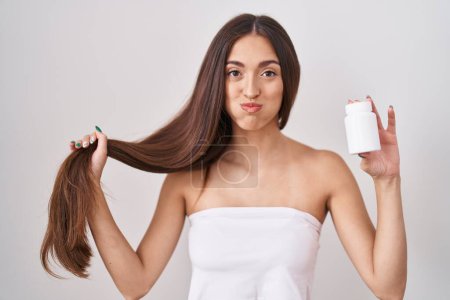 Photo for Young hispanic woman holding hair with hand and pills puffing cheeks with funny face. mouth inflated with air, catching air. - Royalty Free Image