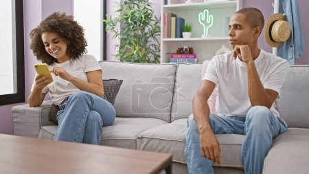 Photo for Beautiful couple unhappy at home, sitting on sofa. girlfriend happily texting, igniting jealousy. their love strained over smartphone use indoors. - Royalty Free Image