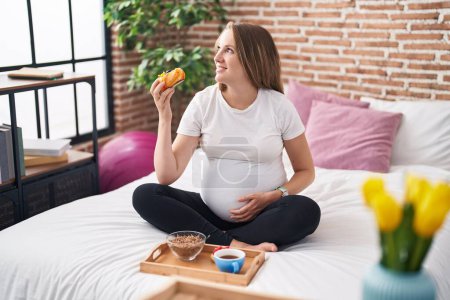 Foto de Mujer embarazada joven teniendo desayuno de regalo sentado en la cama en el dormitorio - Imagen libre de derechos