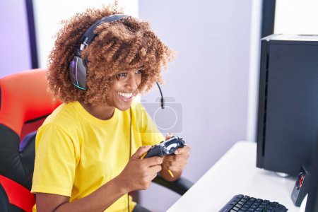 Foto de Mujer afroamericana streamer jugando videojuego usando joystick en sala de juegos - Imagen libre de derechos
